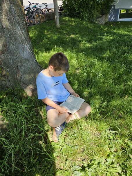 Kinder lesen auf dem Spielplatz, auf der Schaukel, in der Sonne liegend